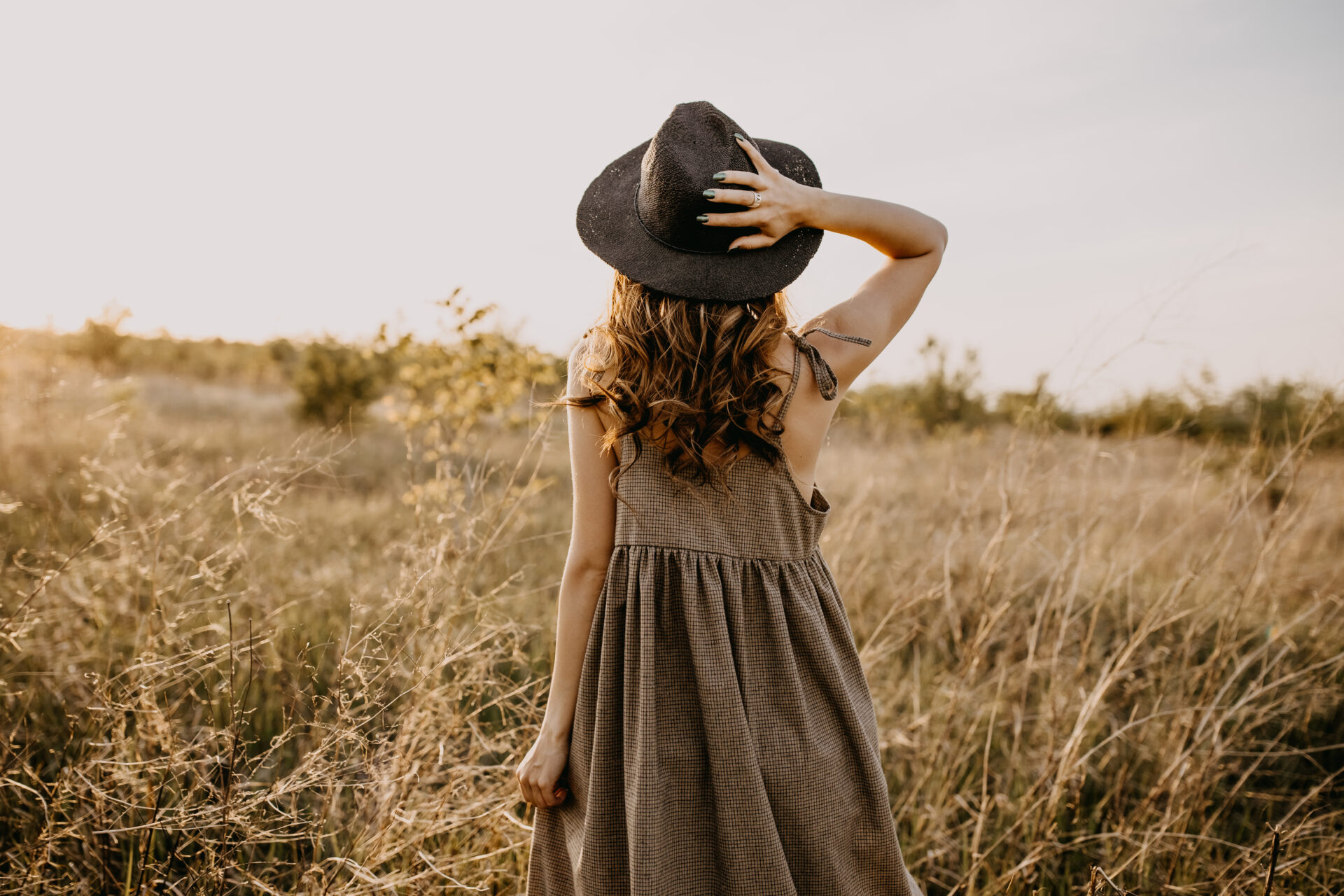 草原に立つ帽子をかぶった女性の後ろ姿