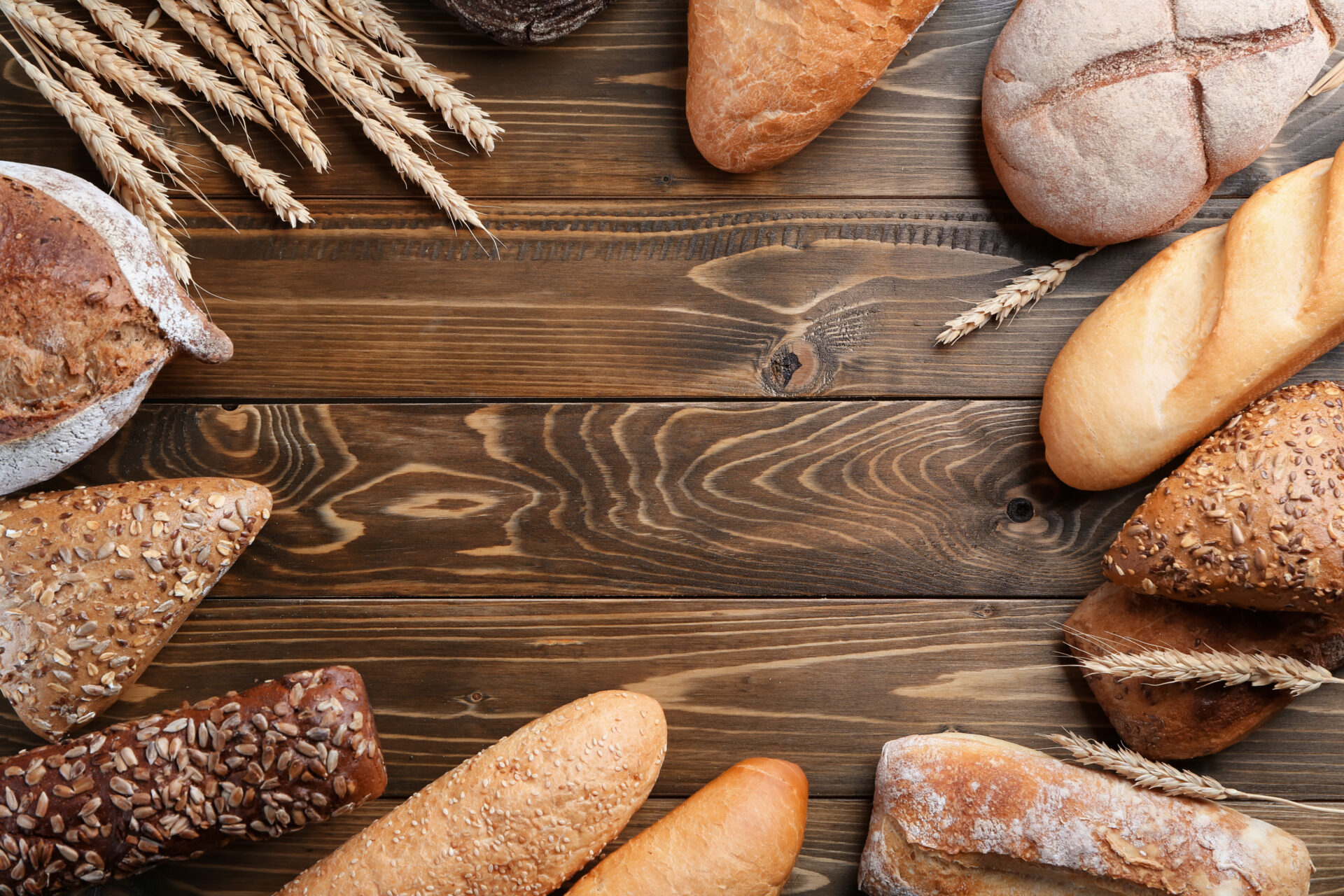 木の板の上に並ぶ色々なパンと小麦