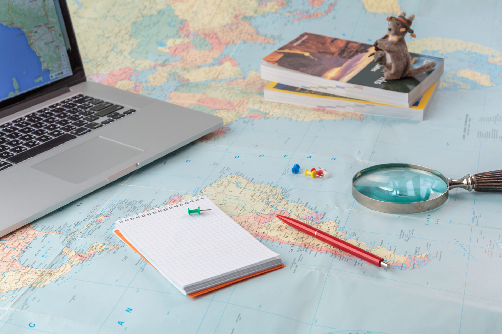 地図の上にパソコン、虫眼鏡、赤鉛筆、メモなど旅行のイメージ