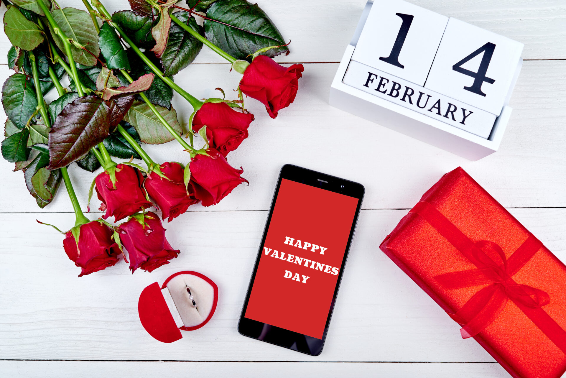 赤いバラの花と赤いプレゼント、バレンタインデーを示すカレンダーにスマホ