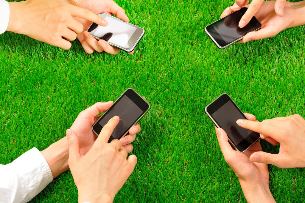 4人が芝の上でスマートフォンを操作する手