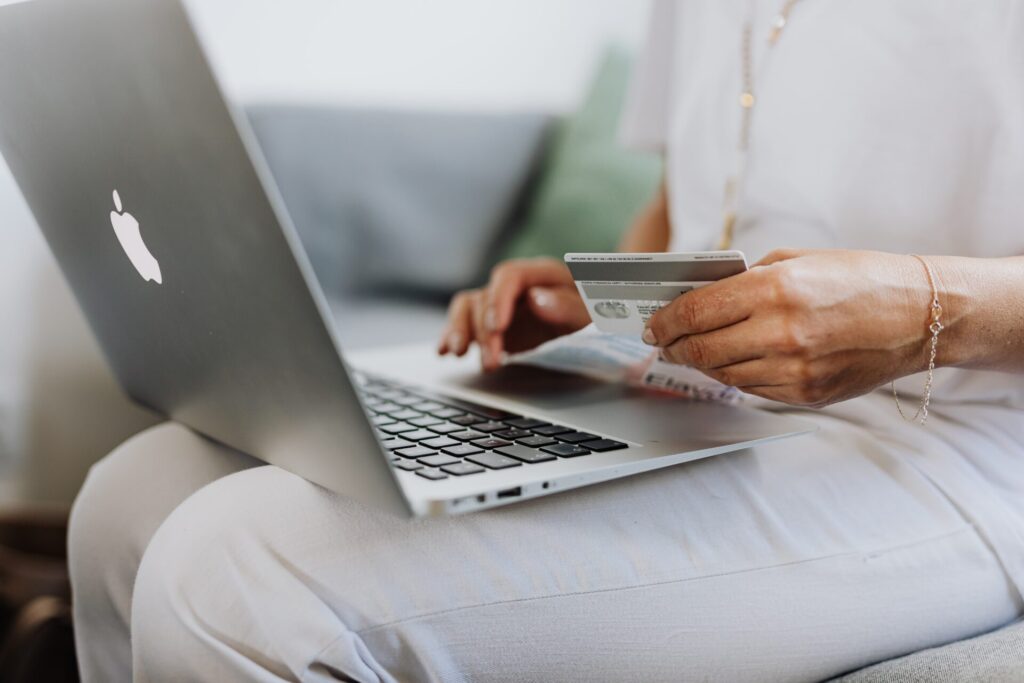 膝の上のパソコンでカード片手にネットショッピングする女性