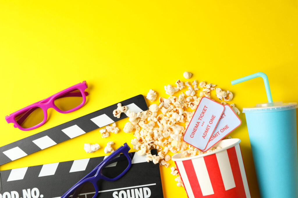 黄色い背景の上に置かれた映画のガチンコ、ポップコーン、映画チケット、サングラス