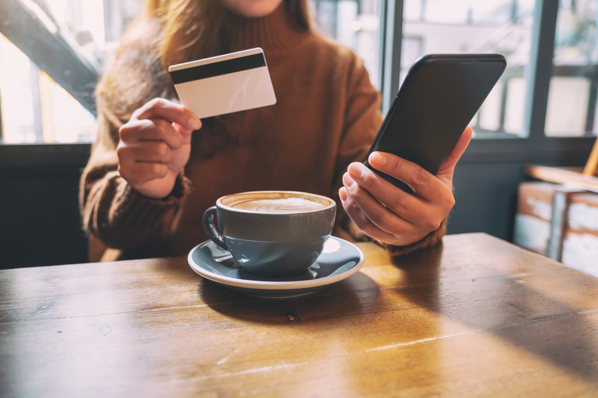 カフェでスマホ片手にクレジットカードを持つ女性