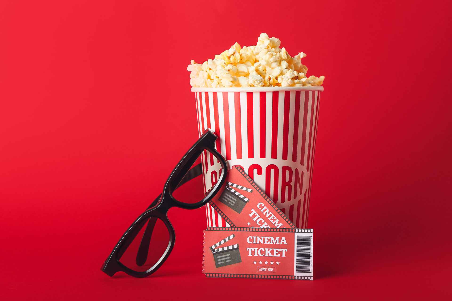 赤い背景の前に置かれたポップコーンと映画チケットと３Dグラス