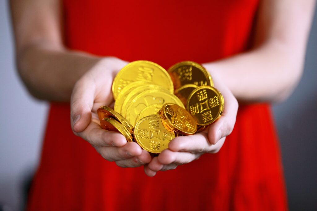 赤いワンピースの女性が両手に持つ金のコイン