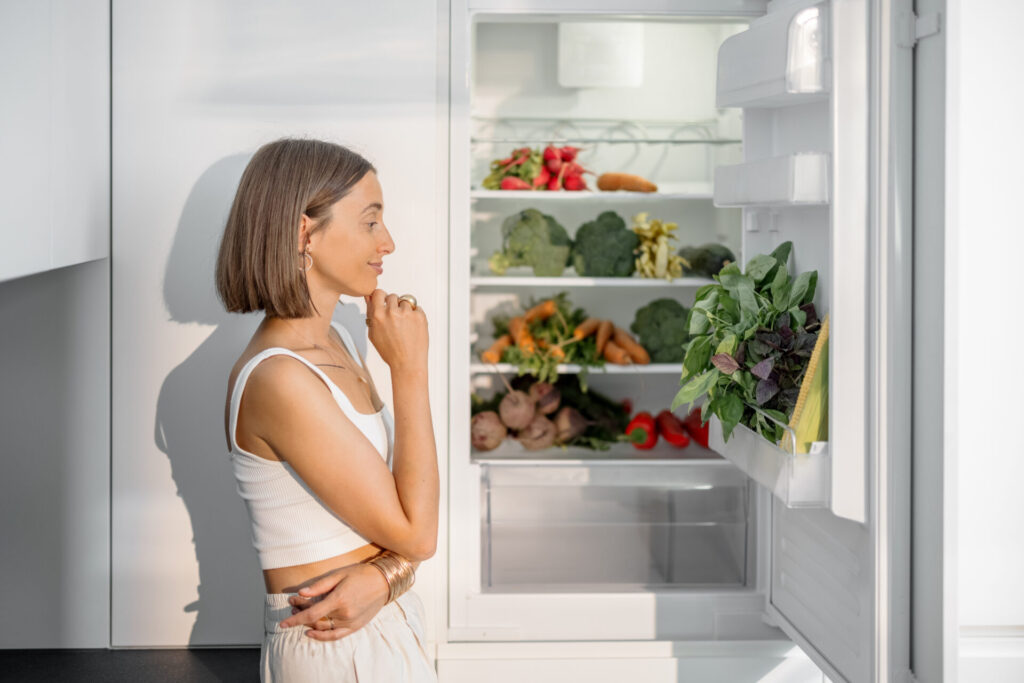 女性が冷蔵庫の中身を見て手を顎に考えている